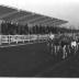 Fotoreportage atletiekwedstrijd: atleten lopen voorbij tribune, Izegem 1957